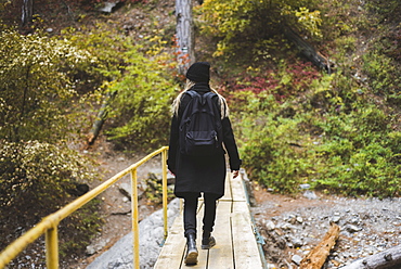 Young woman walking across bridge in forest