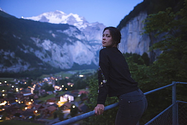 Young woman leaning on railing by mountain and village