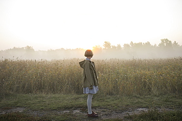 Young woman by field of long grass at sunset