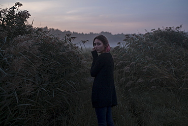 Young woman between bushes at sunset