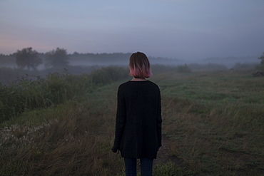 Rear view of young woman in field at sunset