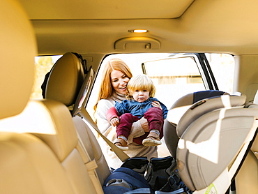 Smiling woman carrying son into car seat