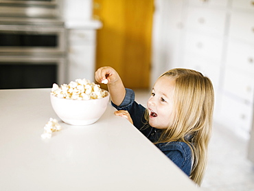 Girl taking popcorn from bowl on kitchen counter