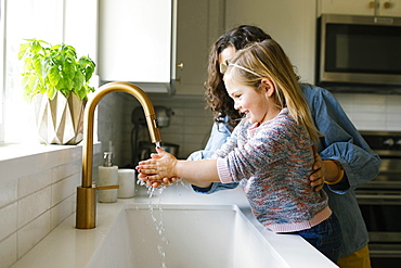 Mother and daughter washing hands in kitchen sink