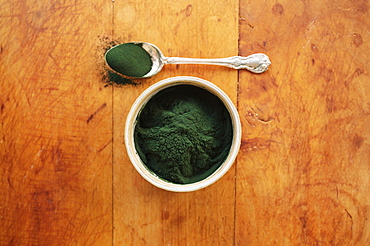 Spirulina in bowl and spoon full against wood