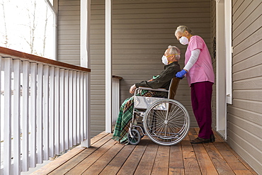 Woman and man in wheelchair wearing protective mask to prevent coronavirus transmission on porch