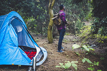 Man holding sticks by tent in forest