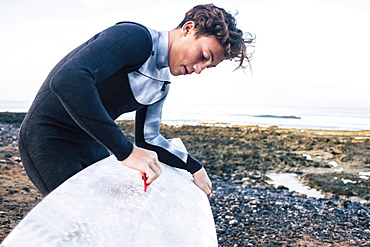 Teenage boy waxing surfboard at beach