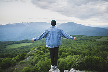 Man standing on cliff by mountain and forest