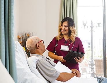 Smiling nurse holding clipboard by senior man in bed