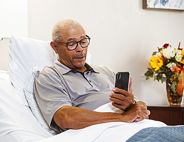 Senior man using smart phone in bed