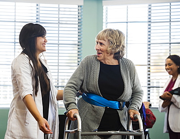 Smiling doctor helping senior woman use walking frame