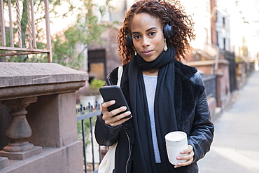 Woman wearing headphones holding smart phone and cup