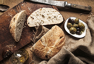 Sliced bread on cutting board by plate of olives