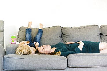 Pregnant woman lying on couch with son (4-5)