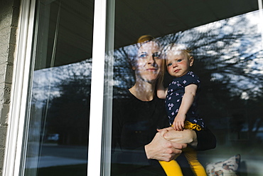 Mother holding daughter (2-3) and looking through window