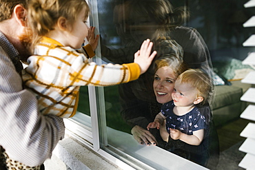 Family with daughters (2-3) visiting through window