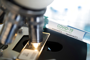 Laboratory microscope with a slide and vial of coronavirus test