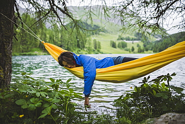 Switzerland, Bravuogn, Palpuognasee, Young woman resting in hammock near Palpuognasee lake in Swiss Alps