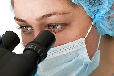 Laboratory technician in face mask looking through microscope