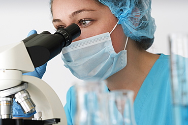 Laboratory technician in face mask looking through microscope