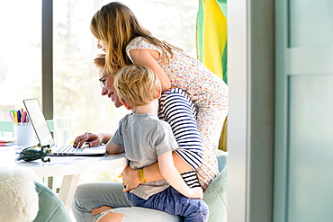 Children (4-5, 6-7) climbing on their mother while she works from home