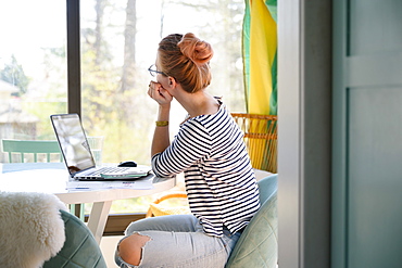 Woman sitting in front of laptop, looking through window