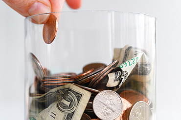 Close-up of fingers putting American cent into jar with coins and banknotes