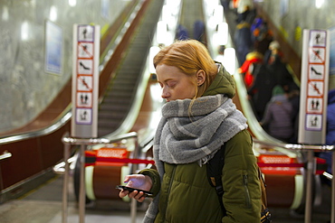 Russia, Novosibirsk, Young woman with smartphone standing by escalator