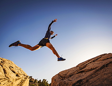 USA, Utah, St. George, Man jumping over rocks while running in landscape