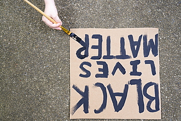 Woman's hand painting Black Lives Matter sign on cardboard