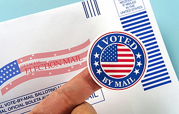 Human finger holding sticker above voting mail