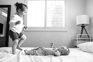 Toddler sister playing on bed with her baby brother