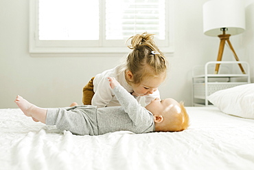 Toddler sister embracing her baby brother on bed