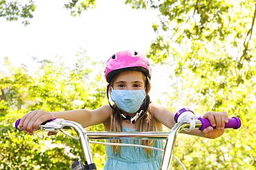 Girl (6-7) wearing flu mask and riding bicycle