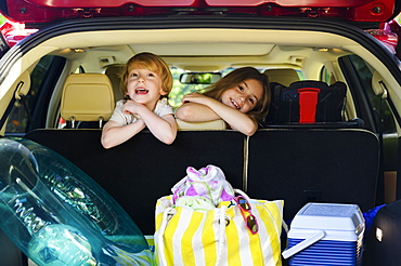 Boy (4-5) and girl (6-7) sitting in car ready for vacation trip