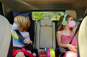 Masked boy (4-5) and girl (6-7) listening to music in car