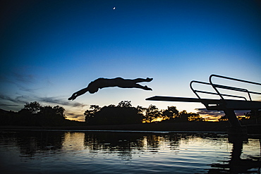 USA, Utah, Salem, Teenage girl (14-15) jumping from pier into lake at dusk