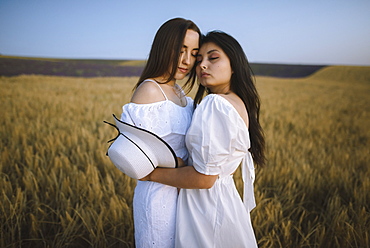 France, Women in white dresses embracing in field