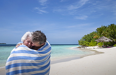 Indian Ocean, Maldives, Ari Atoll, Vilamendhoo Island, Happy couple wrapped in striped beach towel on tropical beach