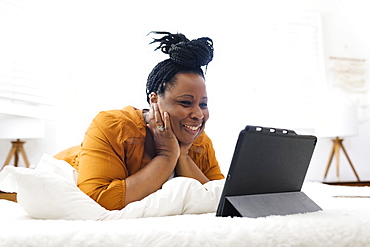 Smiling woman lying on bed and looking at tablet