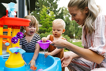 Mother with baby son (18-23 months) and toddler daughter(2-3)playing with water in garden