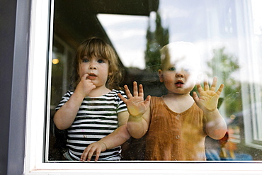 Portrait of toddler girl (2-3) and baby boy (18-23 months) standing behind window