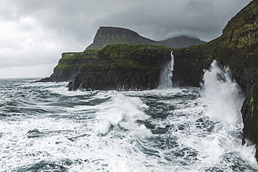 Denmark, Faroe Islands, Gasadalur Village, Mulafossur Waterfalll, Coastline with Mulafossur Waterfall falling into Atlantic Ocean in stormy day