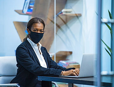 Portrait of businesswoman wearing face mask working on laptop at desk in office