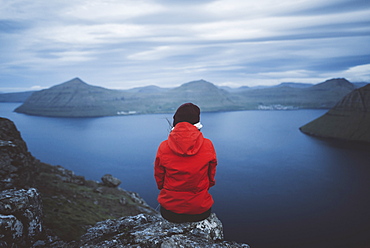 Denmark, Faroe Islands, Klaksvik, Woman sitting on edge of cliff over sea and looking at view