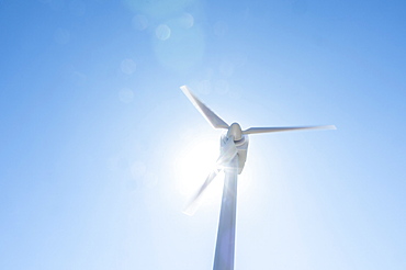 Low angle view of wind turbine against blue sky and sun