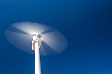 Low angle view of wind turbine spinning against blue sky