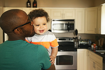 Father kissing baby in kitchen