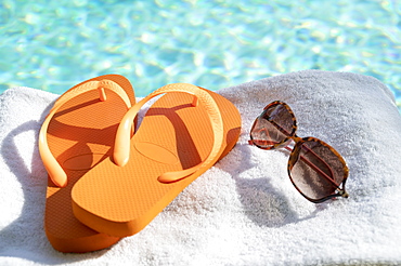 Orange flip flops and sunglasses on towel at poolside